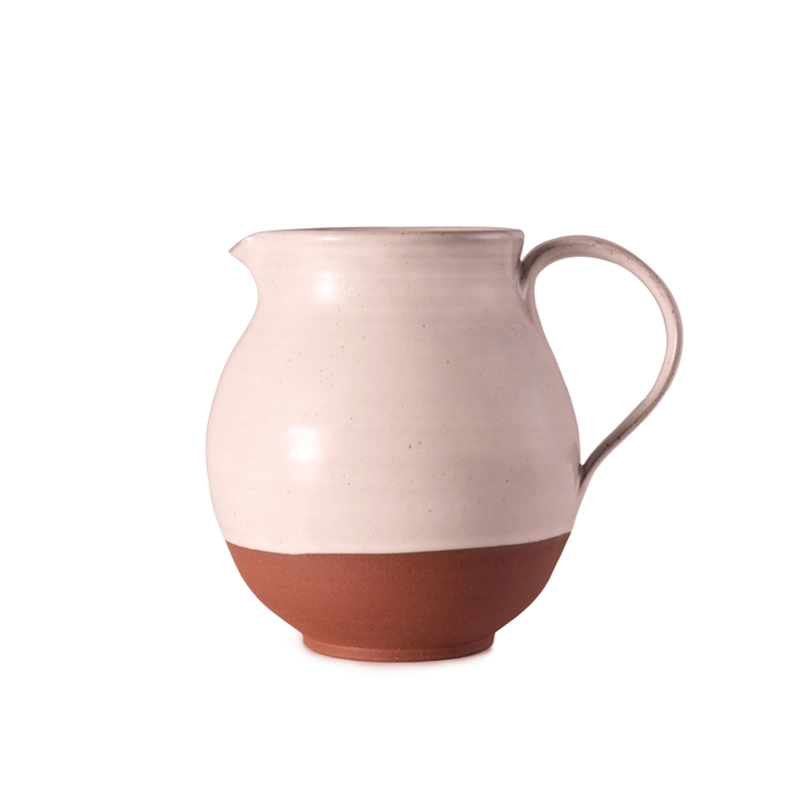 Perfect Hideaways: A handcrafted ceramic jug with a rounded silhouette, finished in a soft cream glaze and exposed terracotta base, featuring a curved handle and spout for easy pouring. Perfect Hideaways shop
