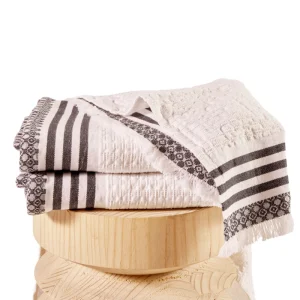 Perfect Hideaways: A close-up of folded white Danakil Waffle Towel with black striped and patterned borders, neatly displayed on a rounded wooden stool. Perfect Hideaways shop