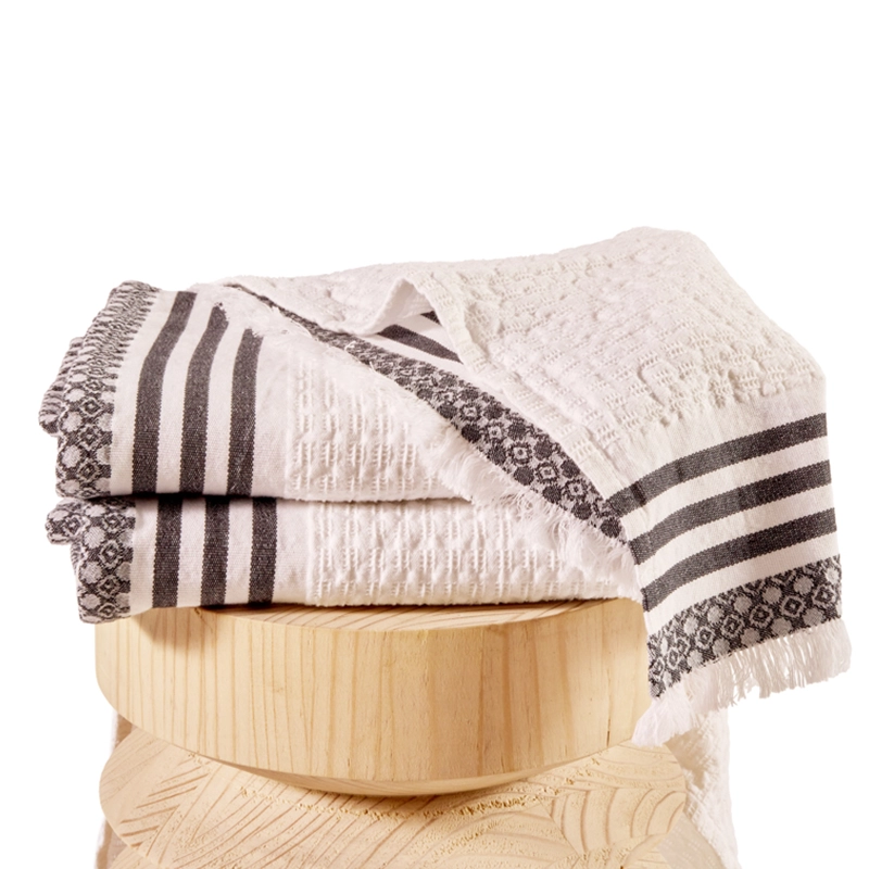 Perfect Hideaways: A close-up of folded white waffle-weave towels with black striped and patterned borders, neatly displayed on a rounded wooden stool. Perfect Hideaways shop