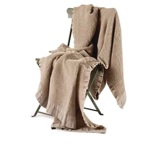 Perfect Hideaways: A textured sand-coloured linen blanket casually draped over a vintage-style green folding chair, showcasing its soft crinkle finish and relaxed elegance. Perfect Hideaways shop