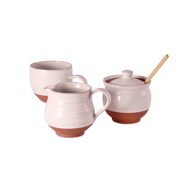 Perfect Hideaways: A ceramic breakfast set including a country milk jug, sugar bowl with wooden spoon, and a matching mug, all with white glazed tops and terracotta bases, displayed against a white background. Perfect Hideaways shop.