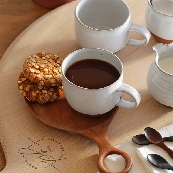 Perfect Hideaways: A styled coffee setting with white Country Round Mugs, one filled with dark coffee and paired with oat biscuits on a wooden board, evoking a cosy, rustic charm. Perfect Hideaway shop