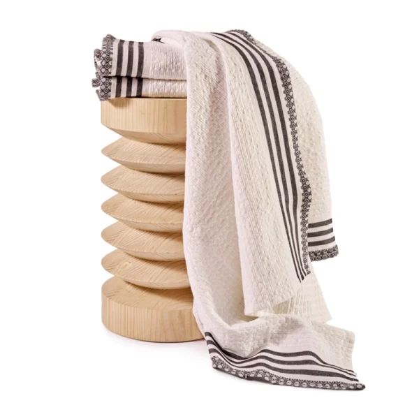 Perfect Hideaways: A full view of a white Danakil Waffle Towel with black woven borders draped over a sculptural wooden stool, showing off its elegant length and detail. Perfect Hideaways shop