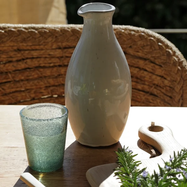 Perfect Hideaways: The ceramic Classic Round Jug styled on a sunlit wooden table with a textured green glass, cutting board and fresh rosemary. The shop