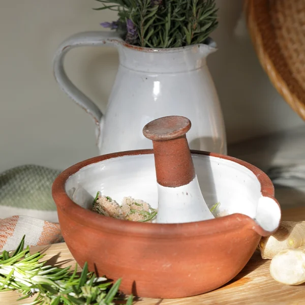 Perfect Hideaways: A ceramic mortar and pestle in use, blending herbs and coarse salt on a wooden surface, with a white jug and fresh rosemary in the background. The shop