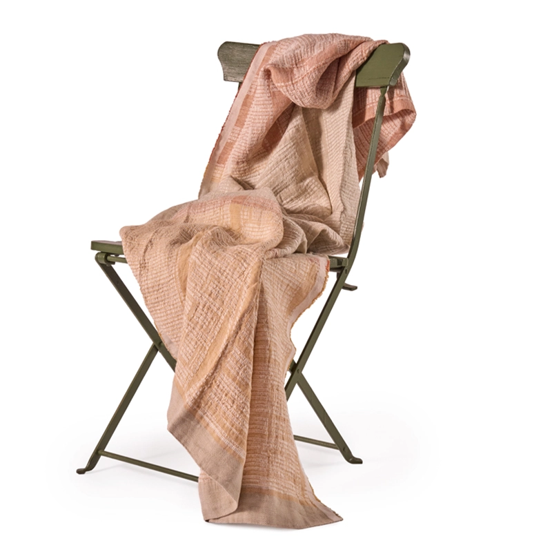 Perfect Hideaways: A soft, textured Dune Bogolan Lounge Throw in warm earthy tones draped elegantly over a sage green folding chair, creating a relaxed and inviting display. Perfect Hideaways shop