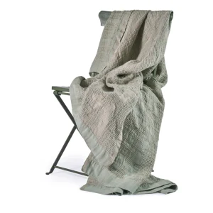 Perfect Hideaways: A soft, Celadon Bogolan Bed Throw draped over a minimalist folding chair, showcasing its intricate woven pattern and relaxed, inviting appeal. Perfect Hideaways shop