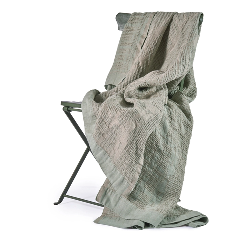 Perfect Hideaways: A soft, Celadon Bogolan Bed Throw draped over a minimalist folding chair, showcasing its intricate woven pattern and relaxed, inviting appeal. Perfect Hideaways shop
