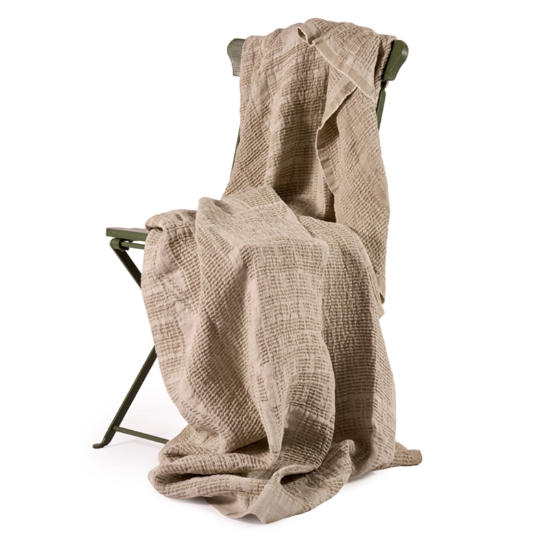 Perfect Hideaways: A soft, natural-toned Bogolan bed throw casually draped over a rustic green metal chair, showcasing its textured weave and relaxed, organic charm. Perfect Hideaways shop