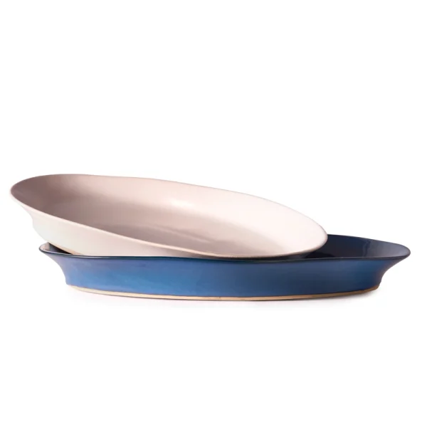 Perfect Hideaways: A set of two oval ceramic platters, one in soft matte white and the other in glossy deep blue, stacked neatly to display their artisanal curves and elegant craftsmanship. The shop