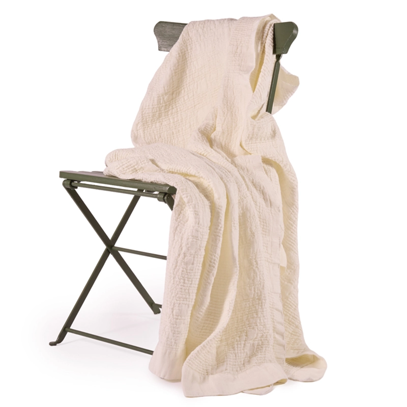 Perfect Hideaways: A soft cotton Pearl Bogolan Bed Throw casually draped over a green metal folding chair, showcasing its light crinkled texture and relaxed elegance. Perfect Hideaways shop