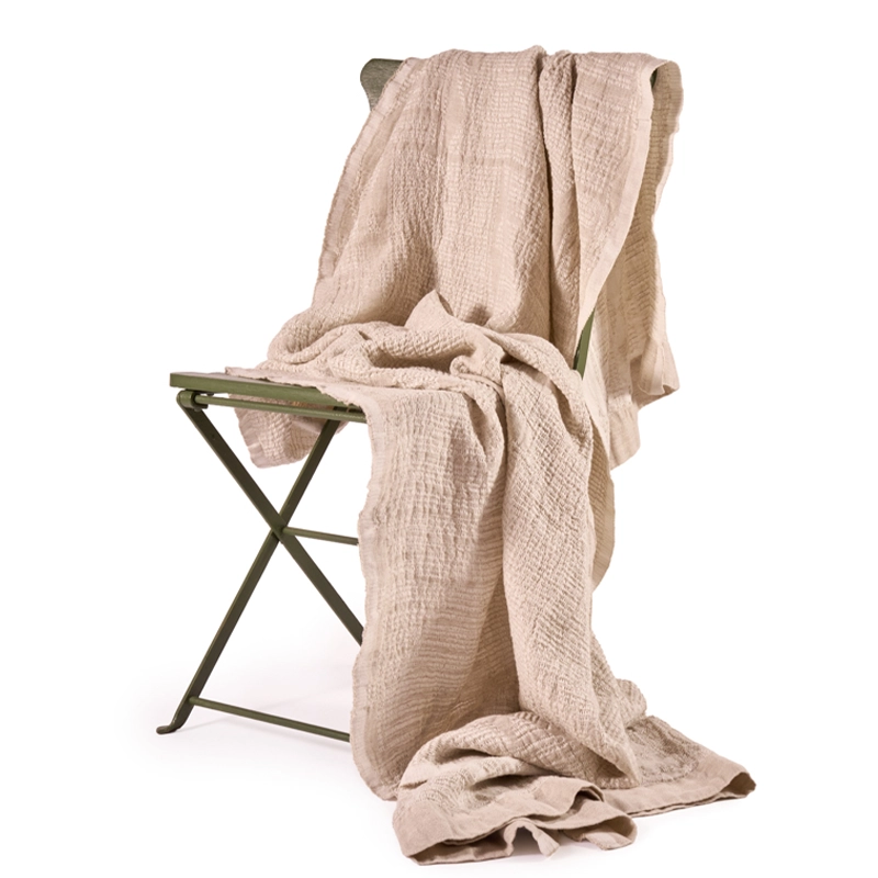 Perfect Hideaways: A Sand Bogolan Bed Throw with a textured finish, casually draped over a metal folding chair for a relaxed, rustic look. Perfect Hideaways shop.