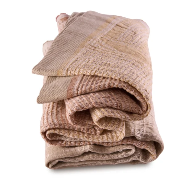 Perfect Hideaways: A neatly folded, Dune Bogolan Lounge Throw showcasing its rich layers of peach, terracotta, and beige hues in a tactile, grid-like texture. Perfect Hideaways shop