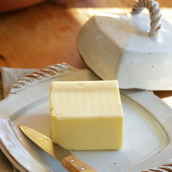 Perfect Hideaways: A creamy block of butter rests on a ceramic butter dish, revealing its earthy-toned lid and hand-twisted rope detail, bathed in soft morning light – Perfect Hideaways shop