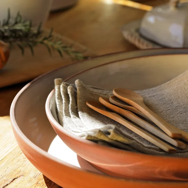 Perfect Hideaways: A close-up of terracotta ceramic Wide Country Lebrillo bowls with a soft blush glaze, stacked and styled with neutral linen napkins and wooden spoons on a sunlit wooden table, Perfect Hideaways shop