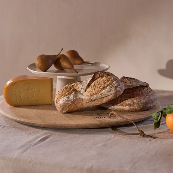 Perfect Hideaways: Rustic table setting with an oak cheese platter displaying crusty bread and cheese, complemented by fresh pears and oranges. Perfect Hideaways shop