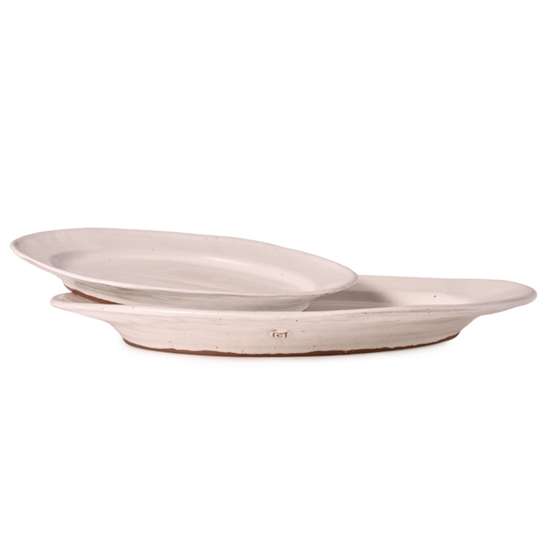 Perfect Hideaways: A set of two classic oval ceramic platters stacked slightly askew to showcase their artisanal shape, off-white glaze, and earthy terracotta bases. Perfect Hideaways shop.