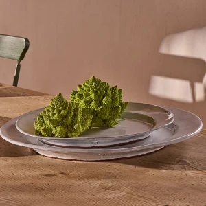 Perfect Hideaways: A rustic wooden table set with a trio of handcrafted oval ceramic platters in neutral tones, elegantly styled with Romanesco broccoli for a natural touch – bathed in warm afternoon light with shadows on a plastered wall. Perfect Hideaways shop.