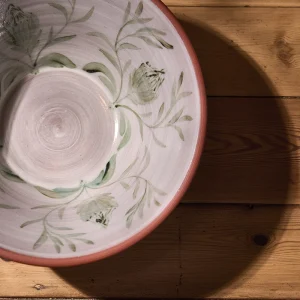 Perfect Hideaways: Handcrafted terracotta bowl displayed on a wooden surface, featuring a glazed interior with delicate green proteas and leaves, creating a soft shadow. Perfect Hideaways shop.