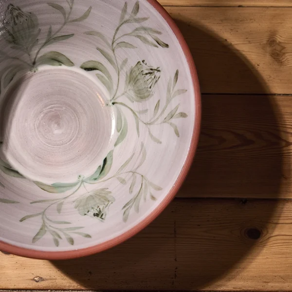 Perfect Hideaways: Handcrafted terracotta bowl displayed on a wooden surface, featuring a glazed interior with delicate green proteas and leaves, creating a soft shadow. Perfect Hideaways shop.