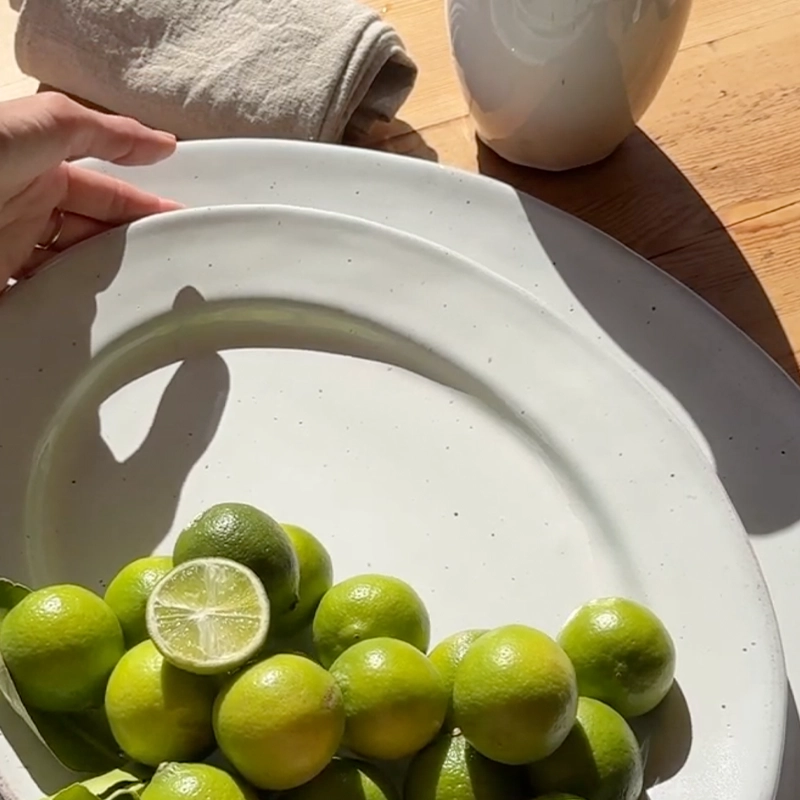 Perfect Hideaways: A cluster of fresh limes, with one sliced to reveal its juicy centre, rests on a handcrafted ceramic platter bathed in soft morning light — a scene of simplicity and natural beauty. Perfect Hideaways shop.