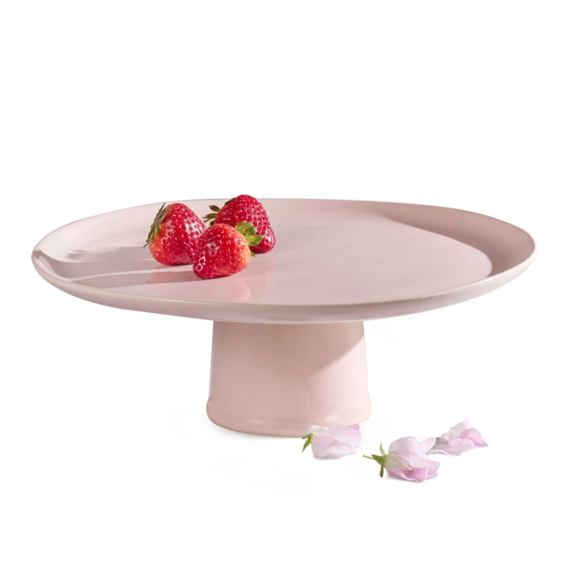 Perfect Hideaways blush pink ceramic cake stand with a minimalist round design, holding a few fresh strawberries and pink flower petals scattered nearby. Perfect hideaways shop.